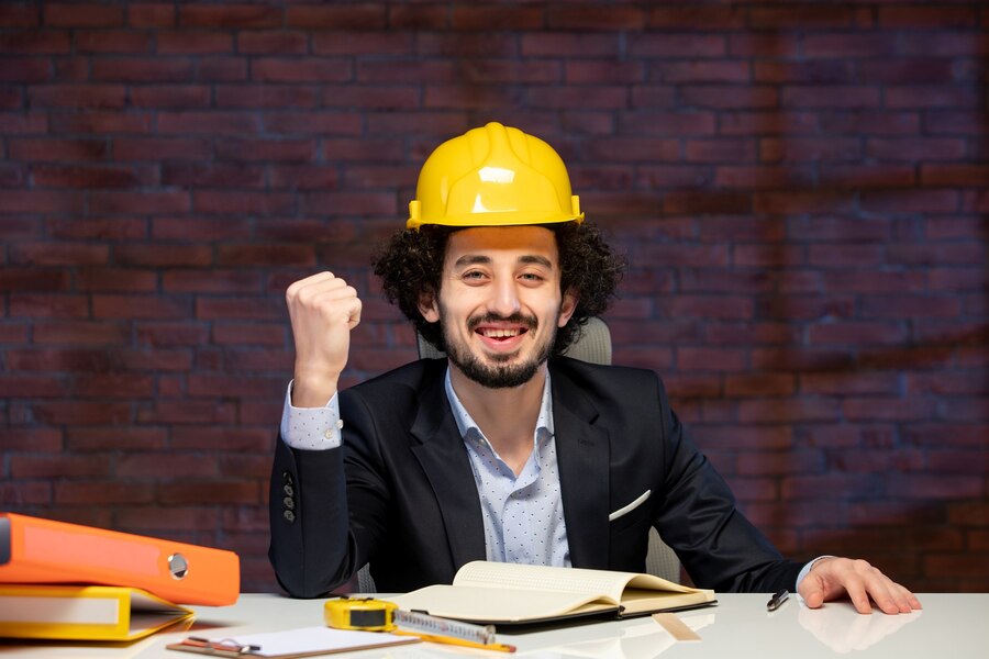 front-view-male-engineer-sitting-working-place-suit-yellow-helmet-plan-business-corporate-job-contractor-work-project-occupation-builder_461922-16201